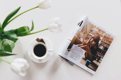 Bild einer Zeitung, einer Tasse Kaffee sowie einer grünen Pflanze mit weissen Blüten, minimalstisch gehalten